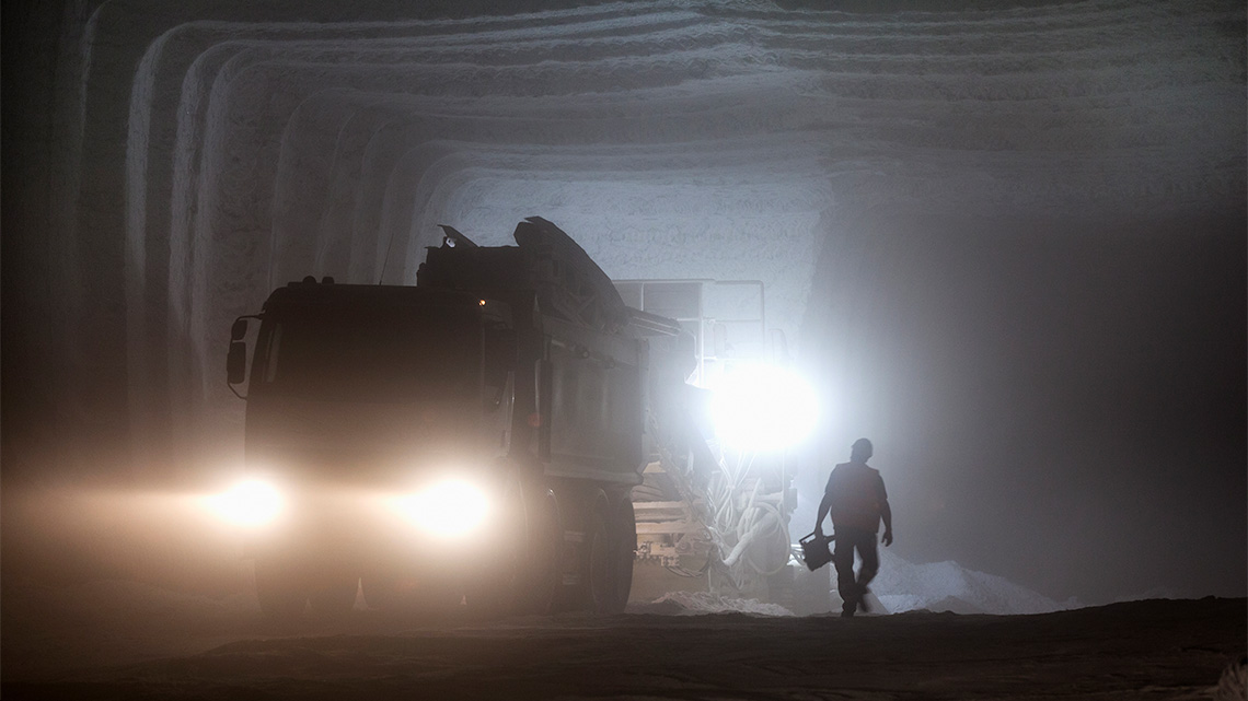A large underground tunnel with a worker and a vehicle lighting the path.