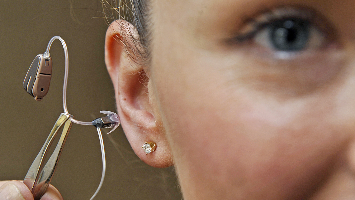 A person holding a hearing aid next to their ear.