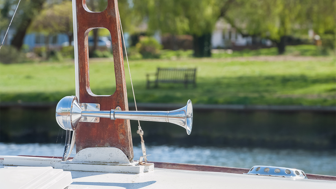 A metal foghorn attached to the railing on the deck of a boat.