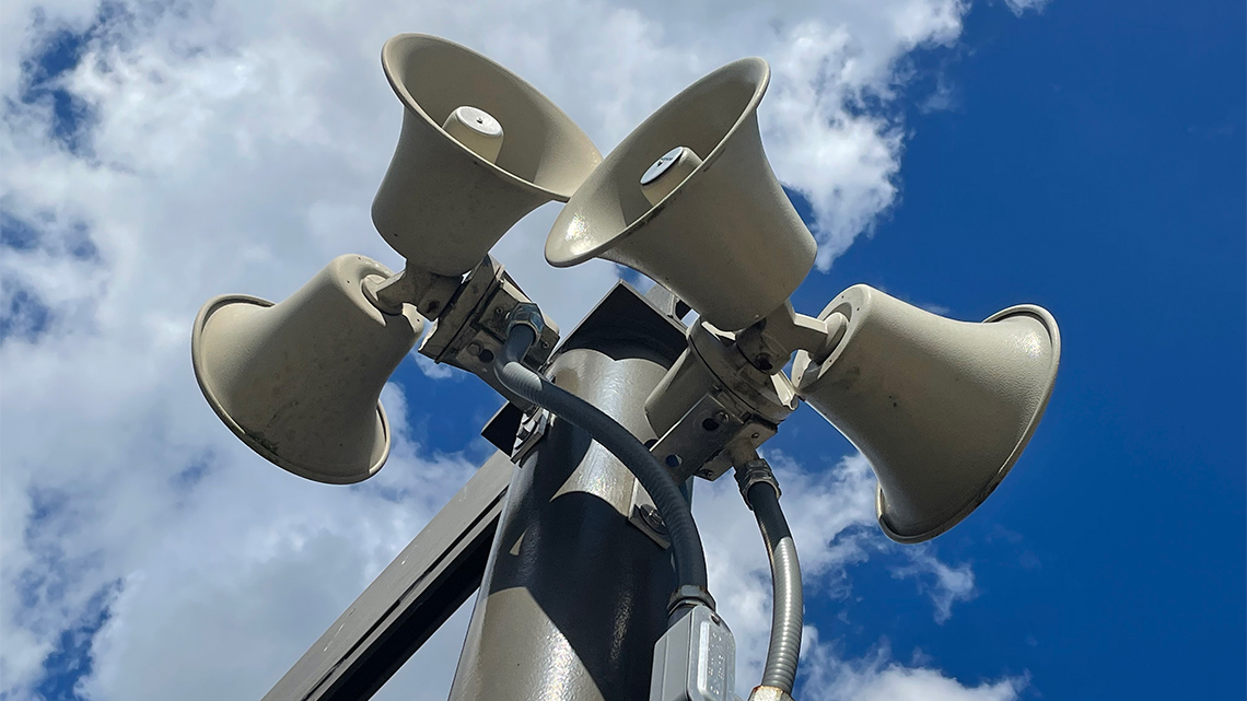 Four metal sirens on the top of a pole, all facing a different direction.