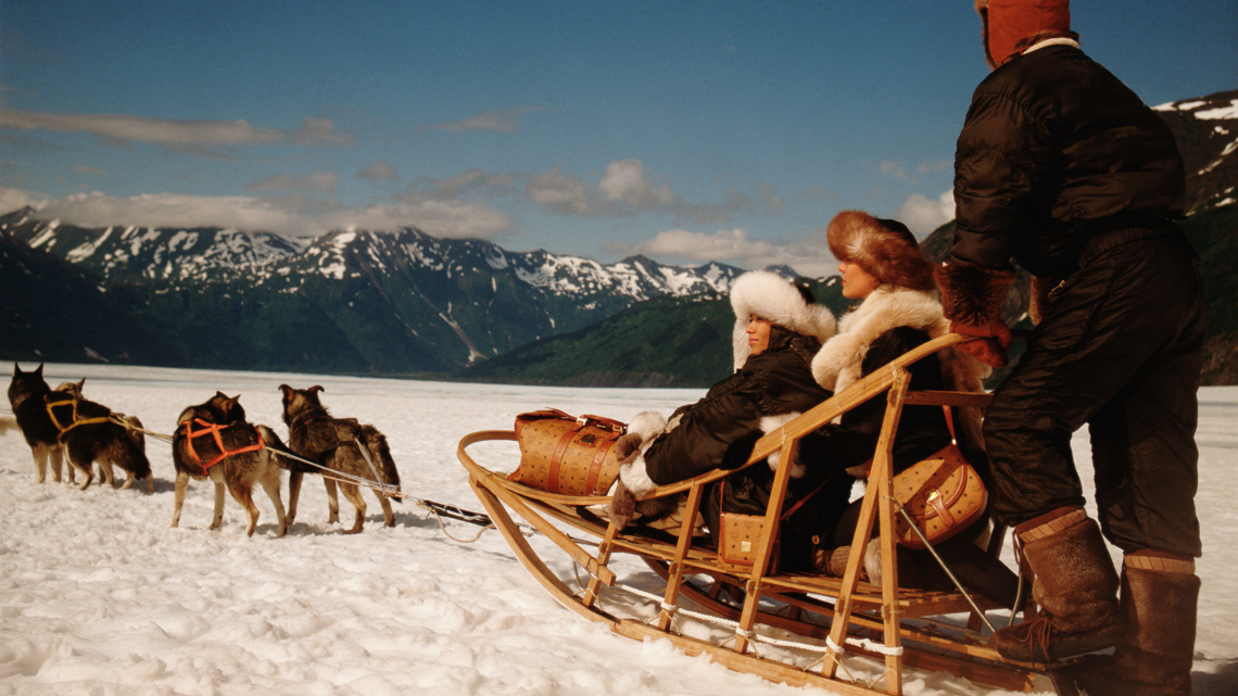 A wooden dog sled carrying people and being pulled by dogs. 
