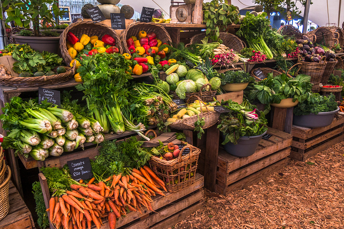 Baskets of vegetables stacked on wooden shelves at a farmers' market.