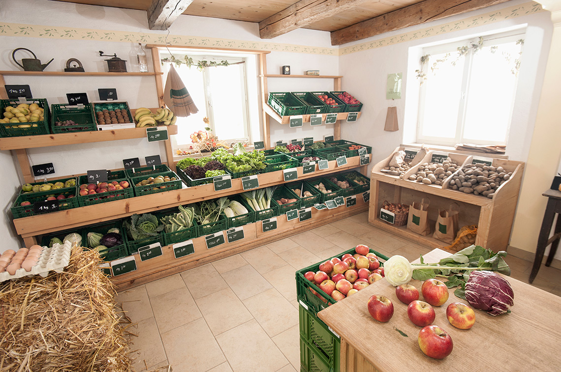 A small vegetable shop with a display of vegetables and fruit on shelves, in baskets and on a table.