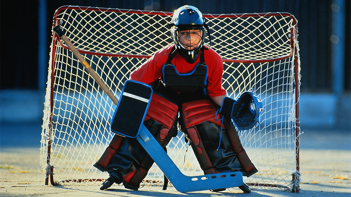 A hockey goalie playing street hockey while wearing proper equipment, such as hockey pads and a helmet.