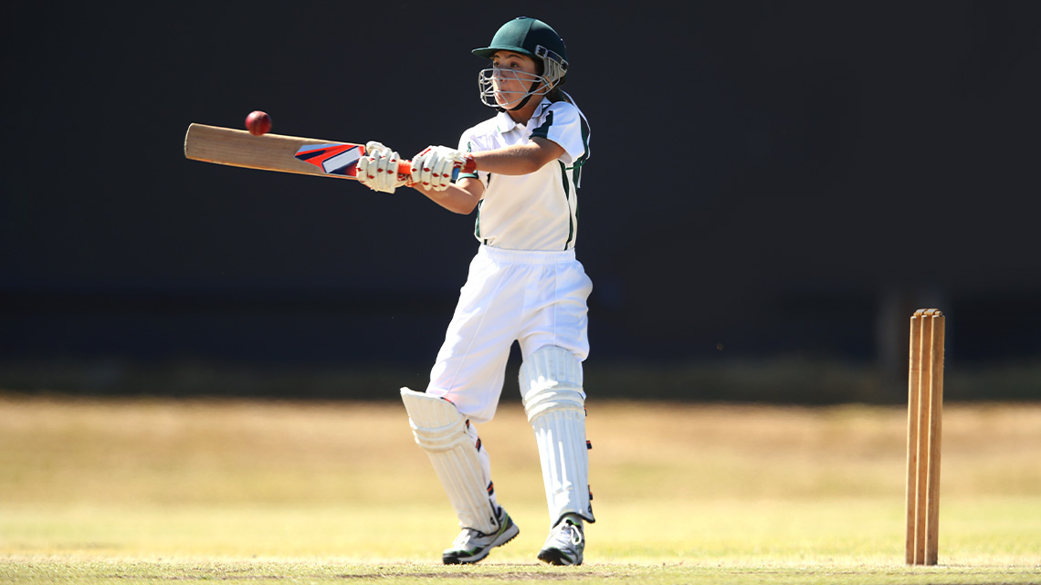 A cricket player with protective knee pads and a helmet hitting the ball with a cricket bat.