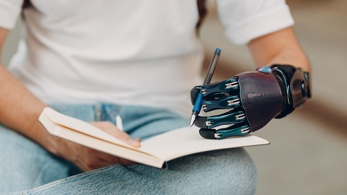 A person with a bionic hand writing in their notebook.