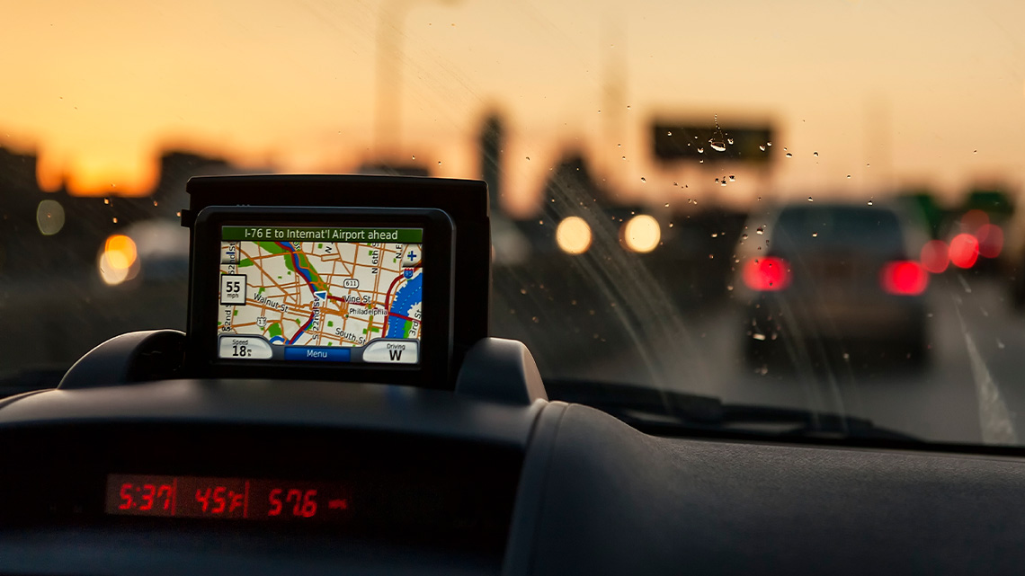 The dashboard of a car on a highway. In the windshield is a drawing of map with a location button on a street.