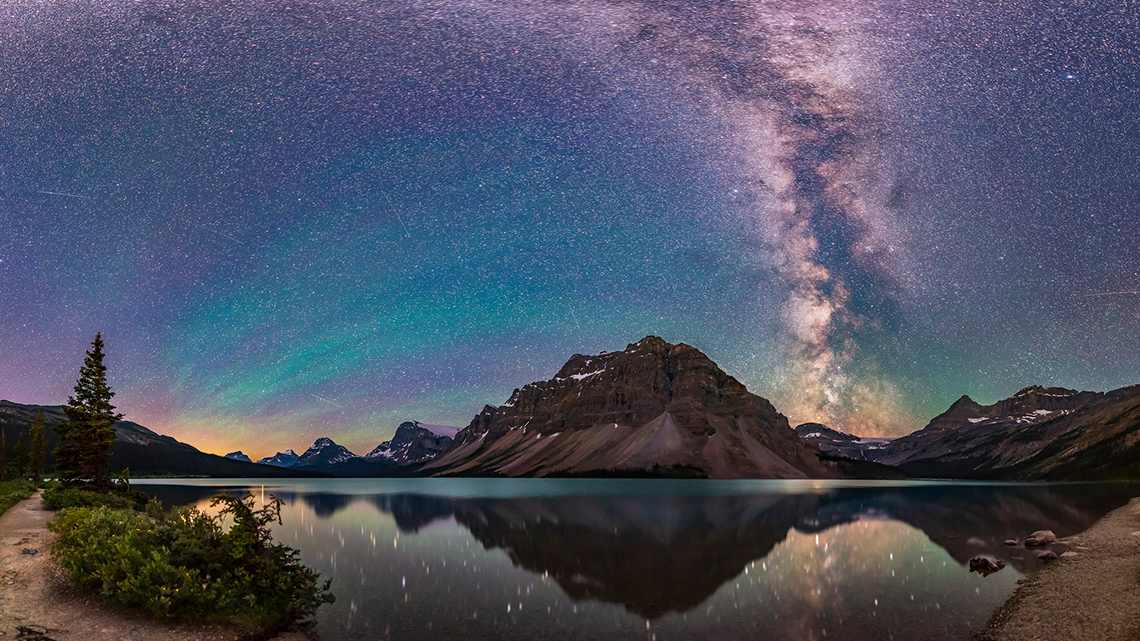 Purple, teal, and pink streaked night sky over mountains and a lake.