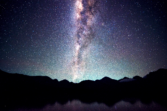 A large glowing pink, teal and purple band of dotted stars and cloud-like streaks of gas cutting across the night sky.