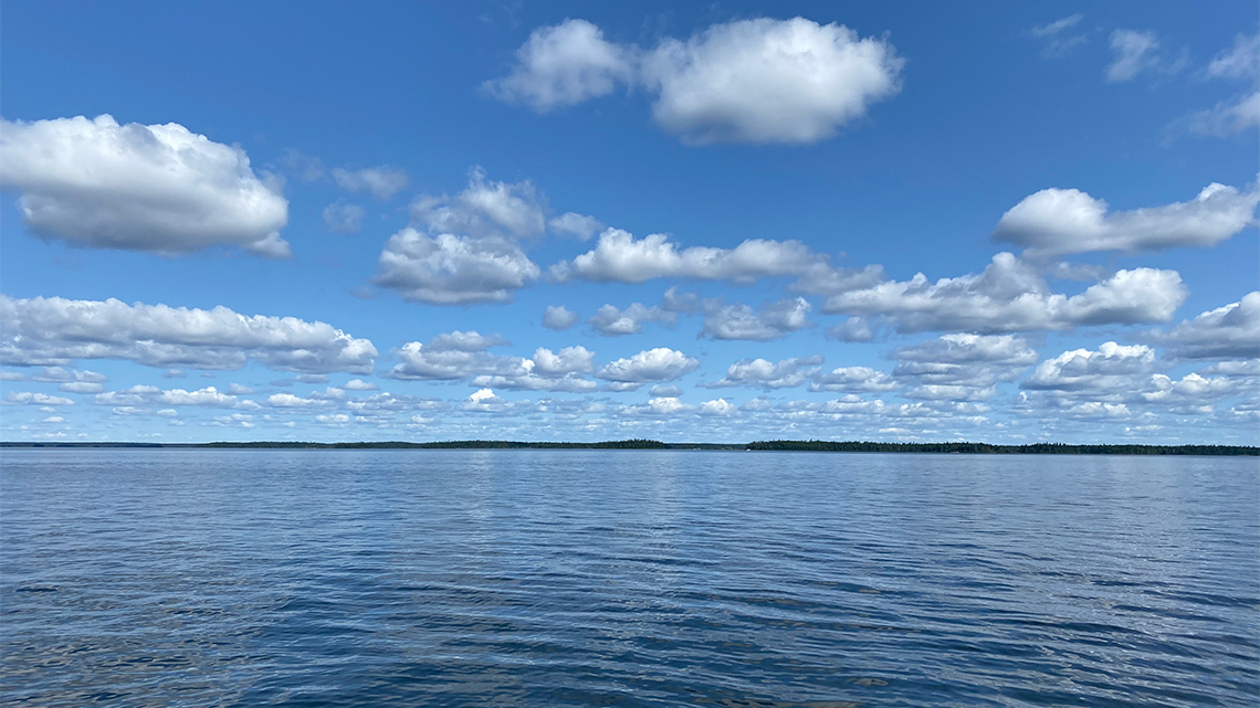 A lake with dark blue water. The sky is clear with a few stray clouds.