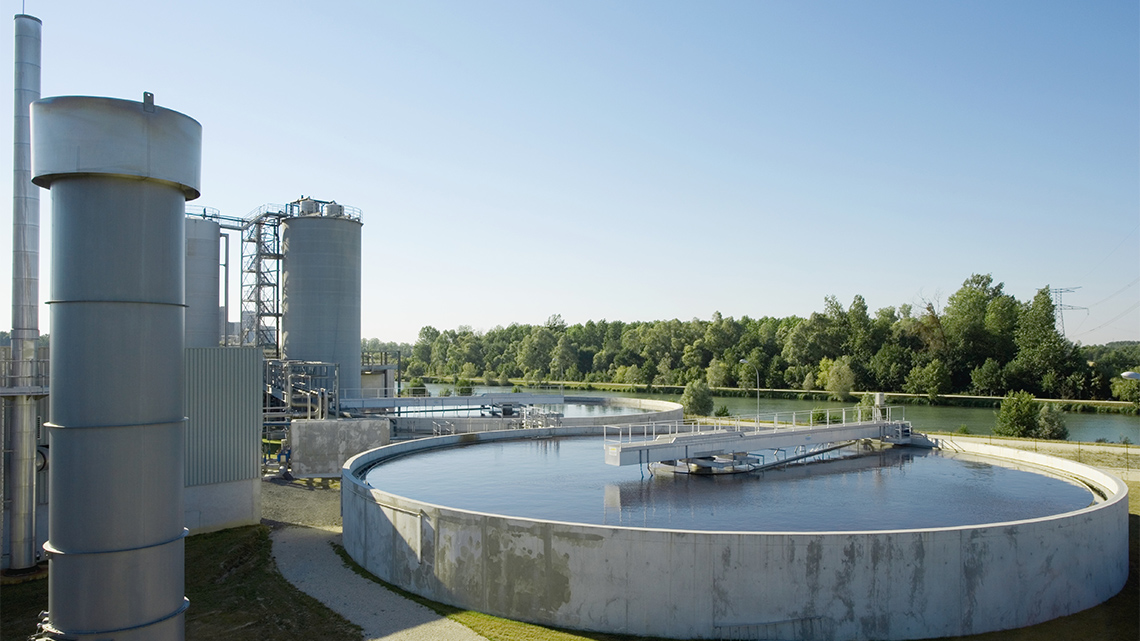 A water treatment plant withs silos and piping that connect to a large concrete pool of water.
