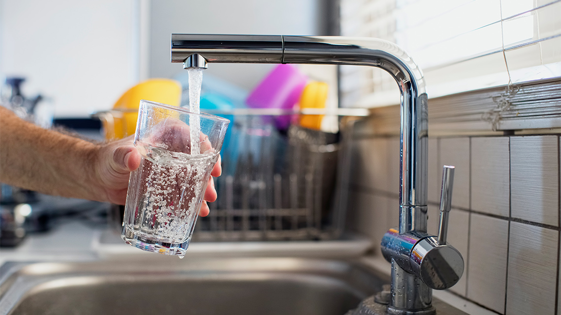 A person filling a glass with water from a tap in a kitchen.