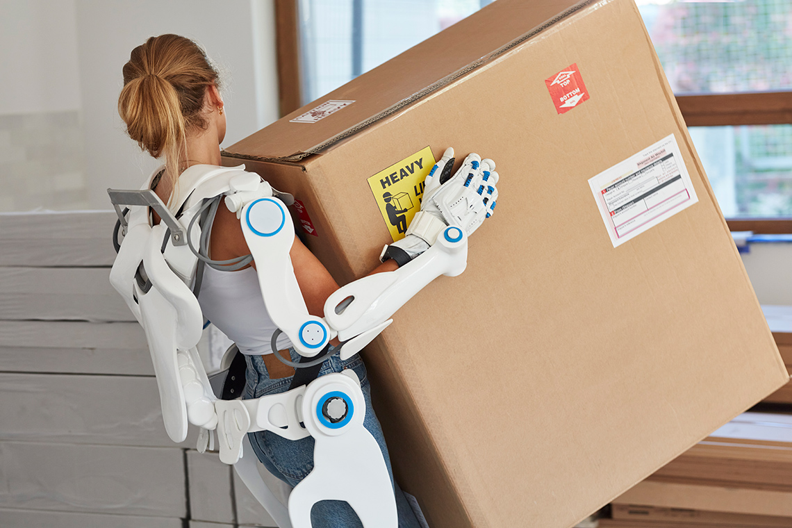A person wearing a robotic suit and carrying a large box.