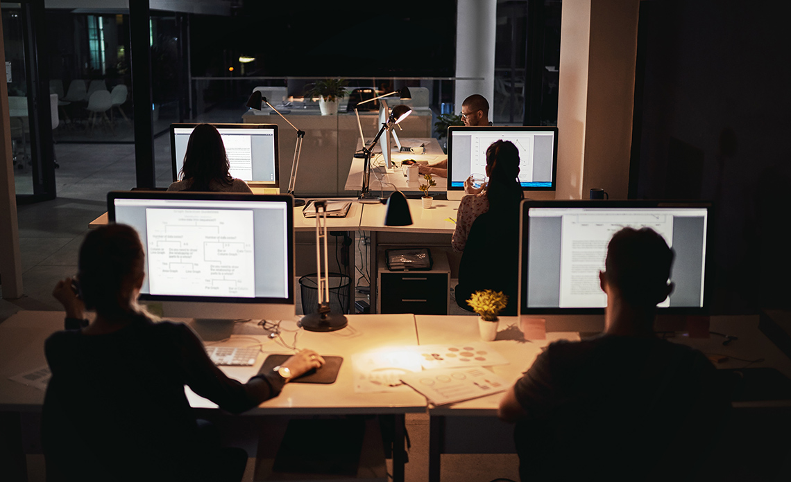 People working in a dark office on their computers with warm lighting around their desks.