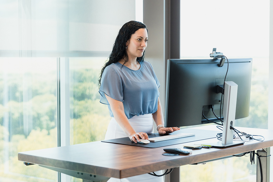 A business woman standing at a raised desk working on her computer.