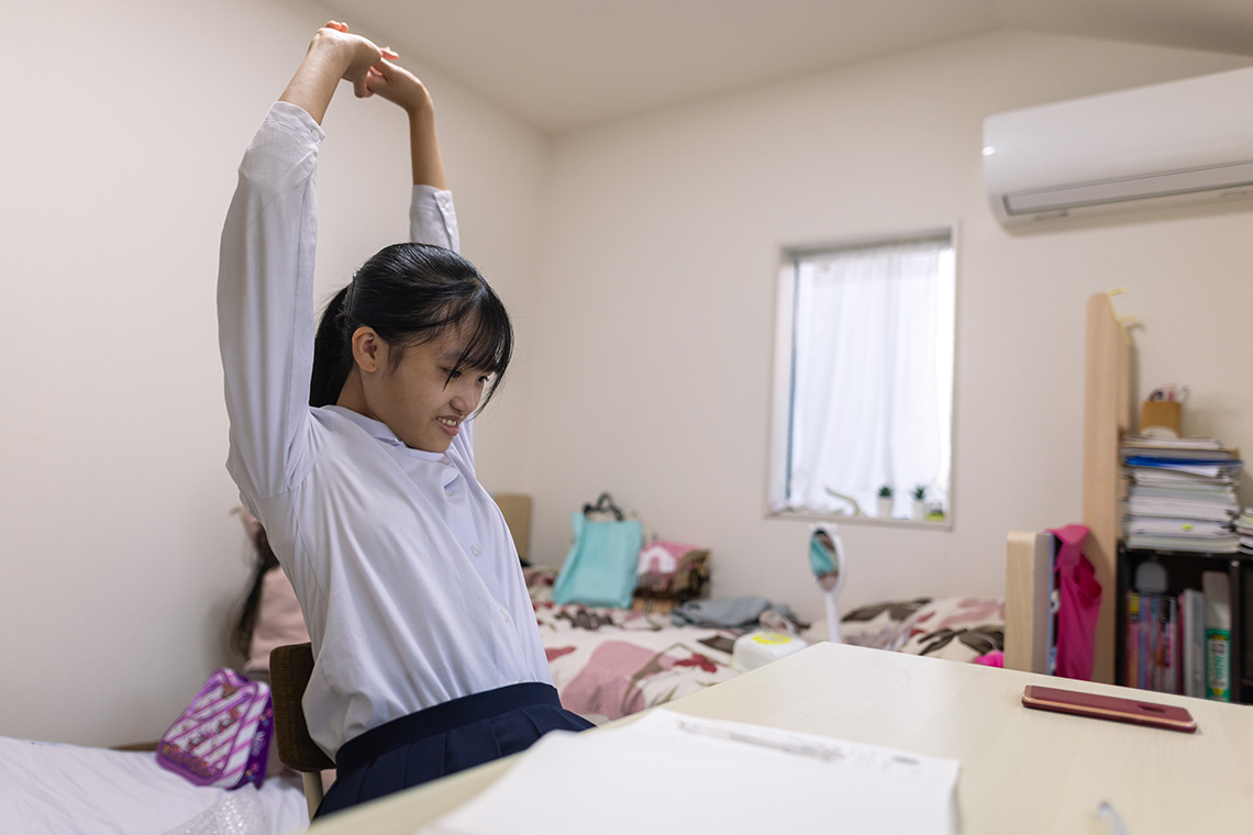 A student at a desk raising their arms to stretch their back.