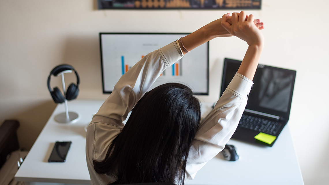 A person at their desk stretching with their arms above their head.