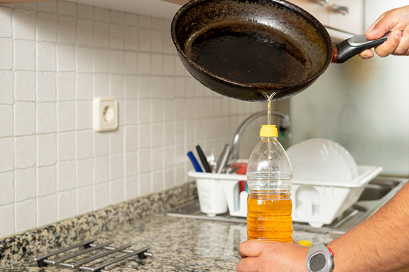 A person pouring used cooking oil from a frying pan into a plastic water bottle.