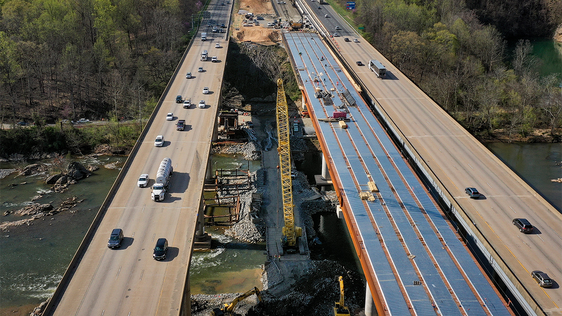 A busy highway spanning a river with five new lanes being constructed.