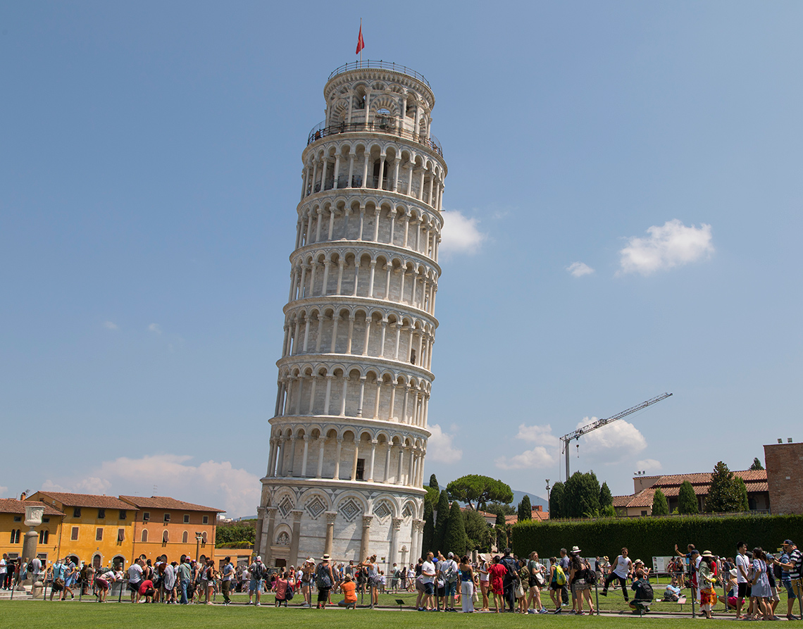 Tourists surround the Learning Tower of Pisa, a seven-story tower leaning at a noticeable angle.