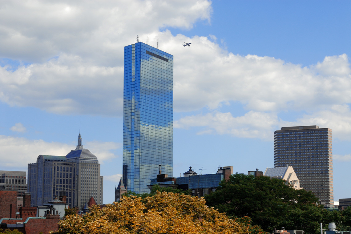 The John Hancock Tower is a large glass tower that rises far above surrounding buildings. Windows are missing from some of the upper levels.