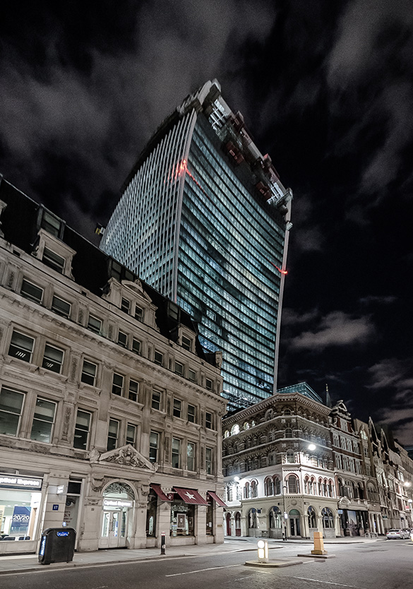 A tall concave glass tower rising above a street and shorter buildings.