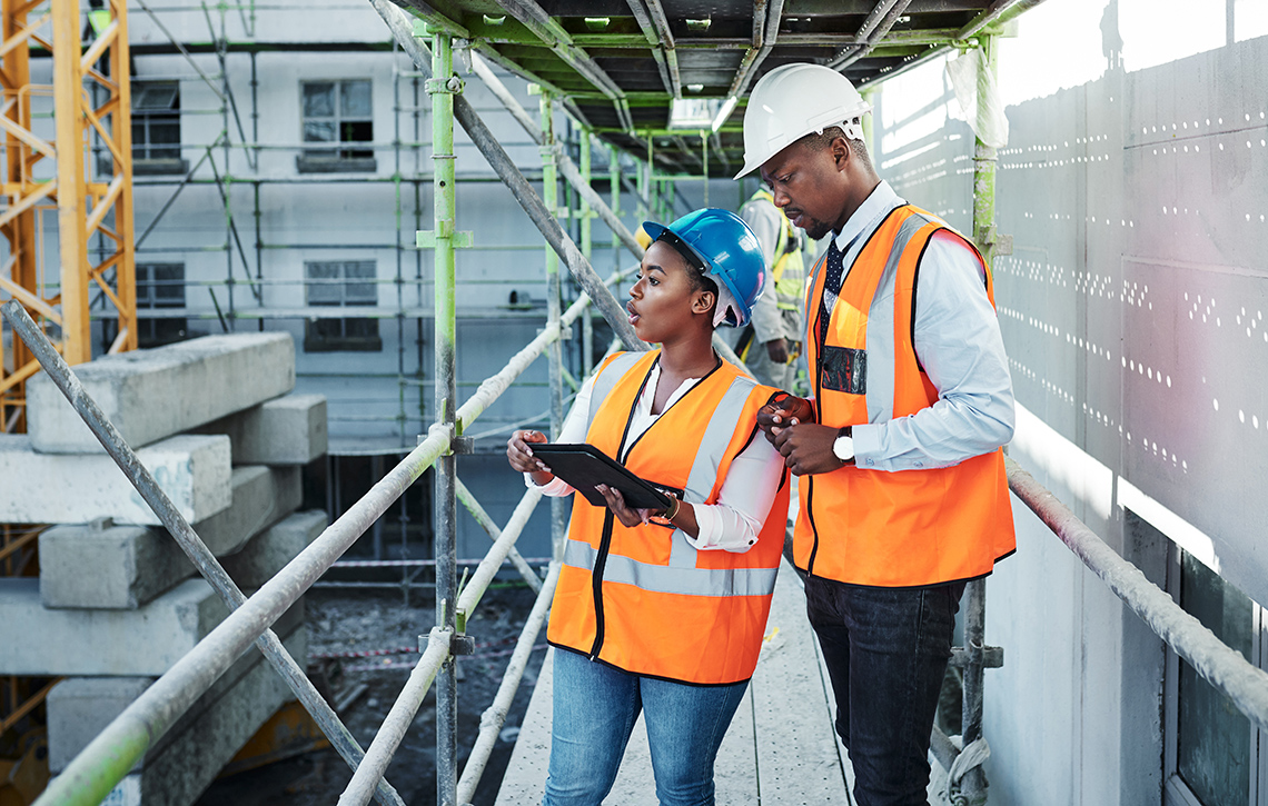 Two engineers inspect a construction site from scaffolding near the base of a crane.