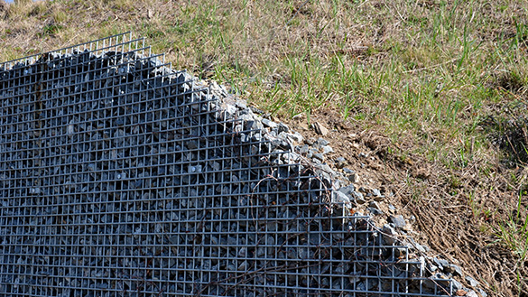 Wiring forming a grate alongside a grassy incline. It adds support to the hill and prevents rocks from spilling from the hill onto the ground.