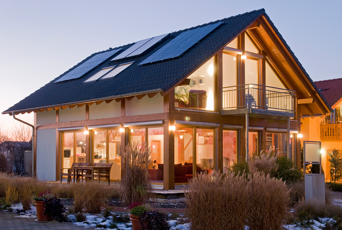 A house with solar panels on the roof and the lights on inside.
