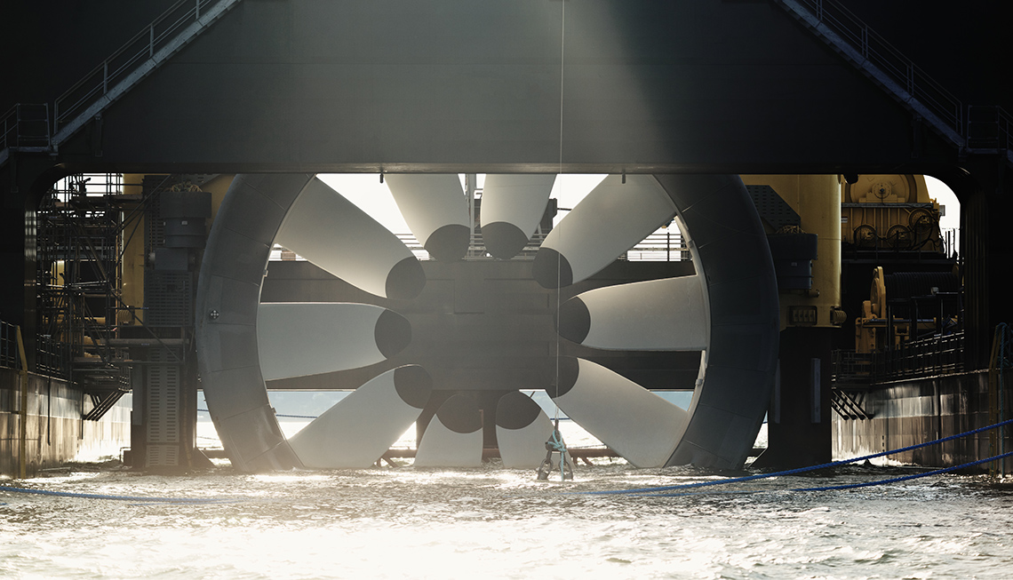 A large tidal turbine connected to machinery and partially submerged in water near a coast.