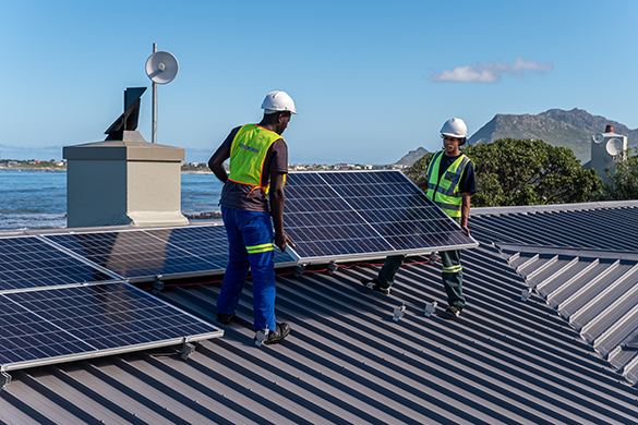 Two workers installing solar panels of the roof of a building.