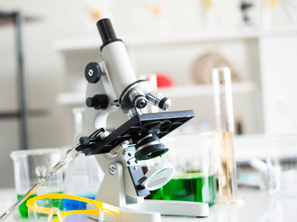 A microscope on a table surrounded with chemicals and safety goggles.