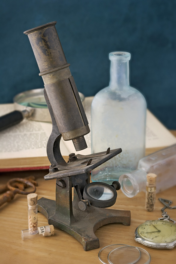 Antique compound microscope with lenses, eyepiece, slide holder, and mirror.