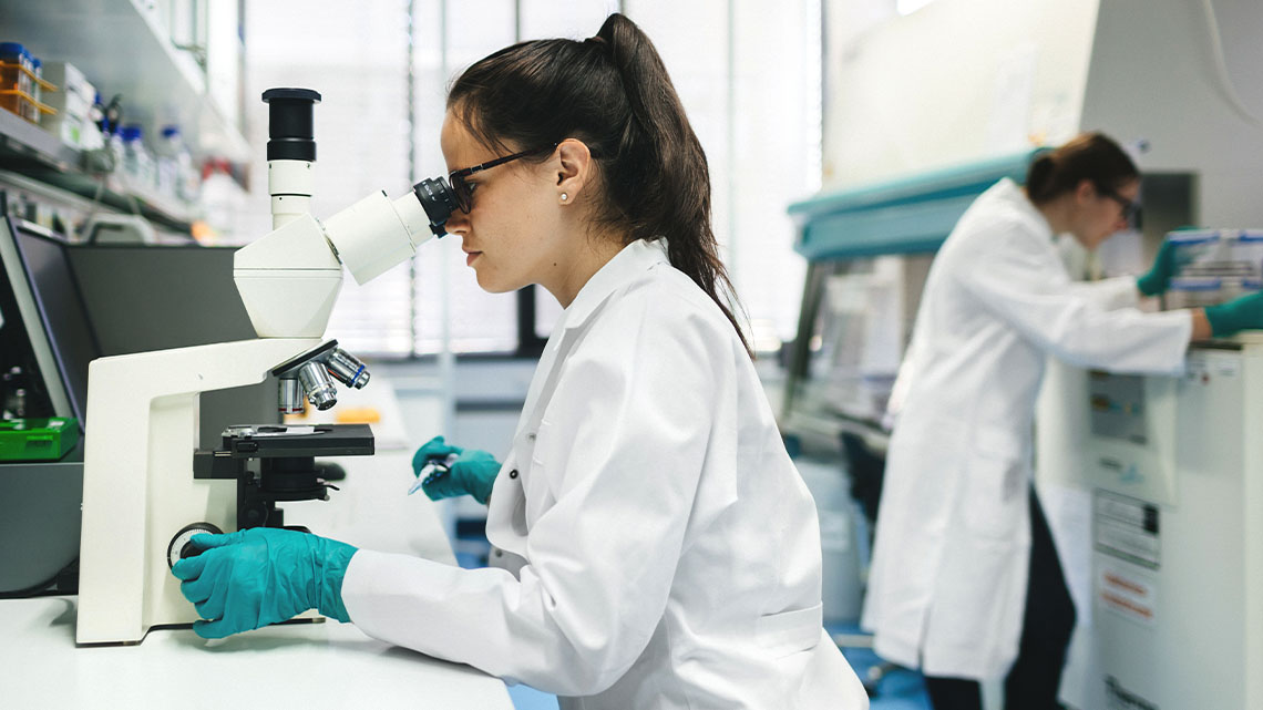 Two researchers in a room, both are looking into microscopes.