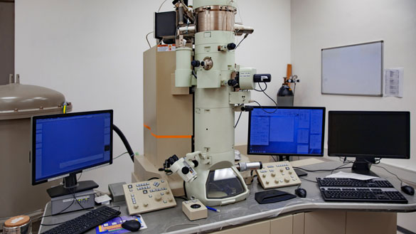 Full Electron Microscope A large cylinder that is an electron microscope sits on a table and is connected to three different computers as well as several different control panels.