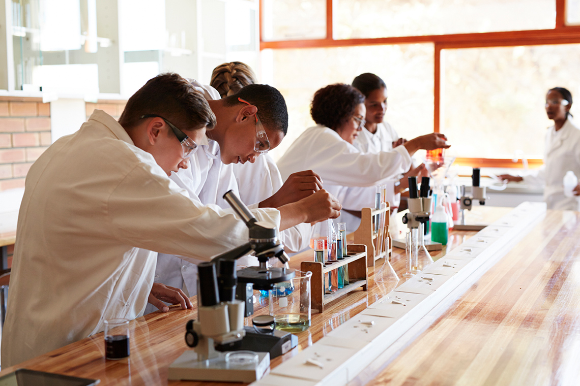 Students working in a science laboratory with test tubs, microscopes and beakers.