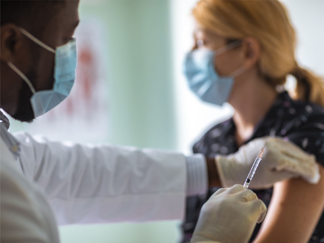 A healthcare worker holding a syringe containing liquid while sanitizing a patient's arm with a cotton swab.