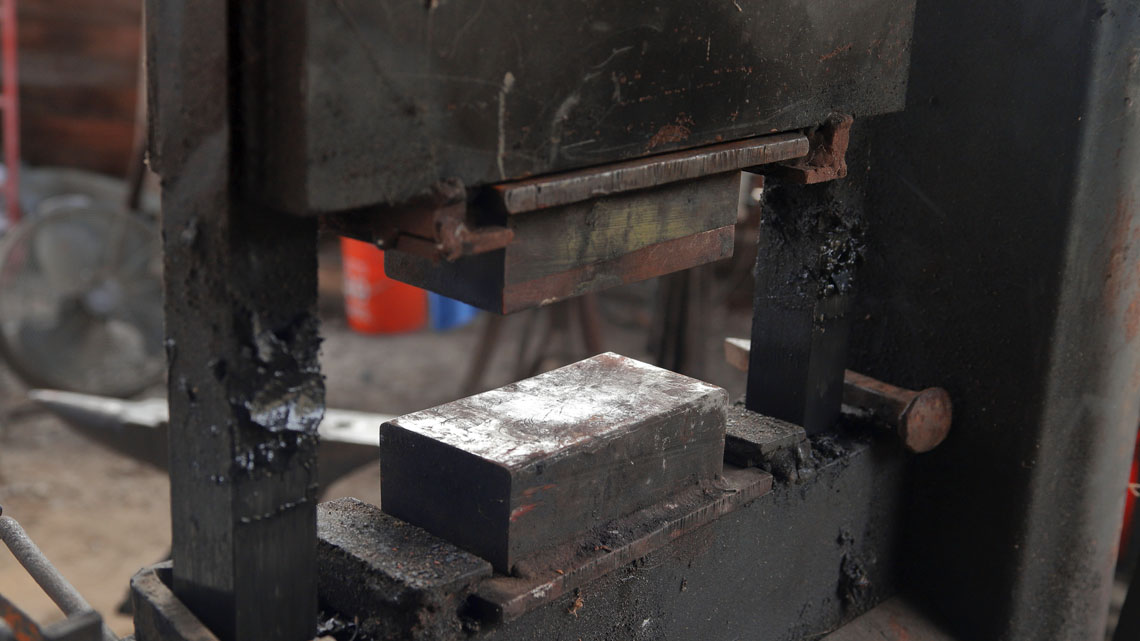 Hydraulic press machine with a solid metal block at the base and a moveable metal block above it controlled by hydraulics.