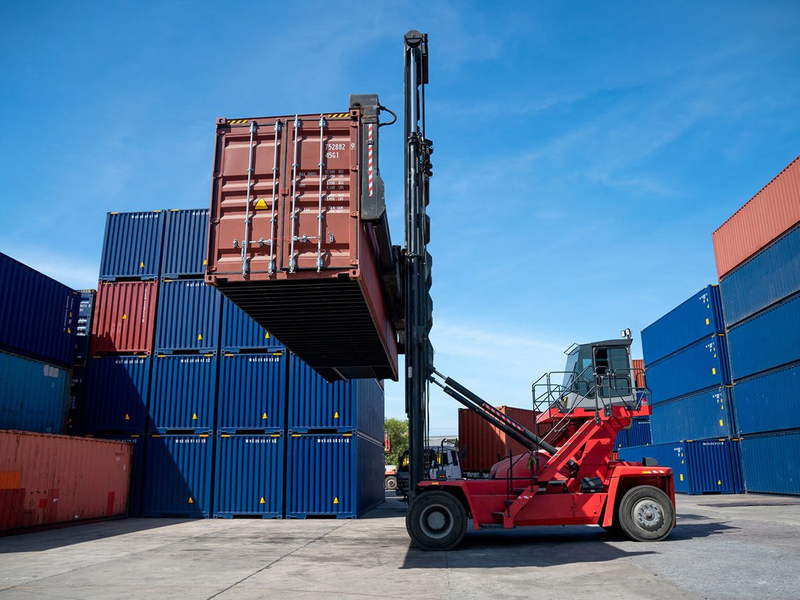 A forklift lifting a shipping container onto a stack of shipping containers.