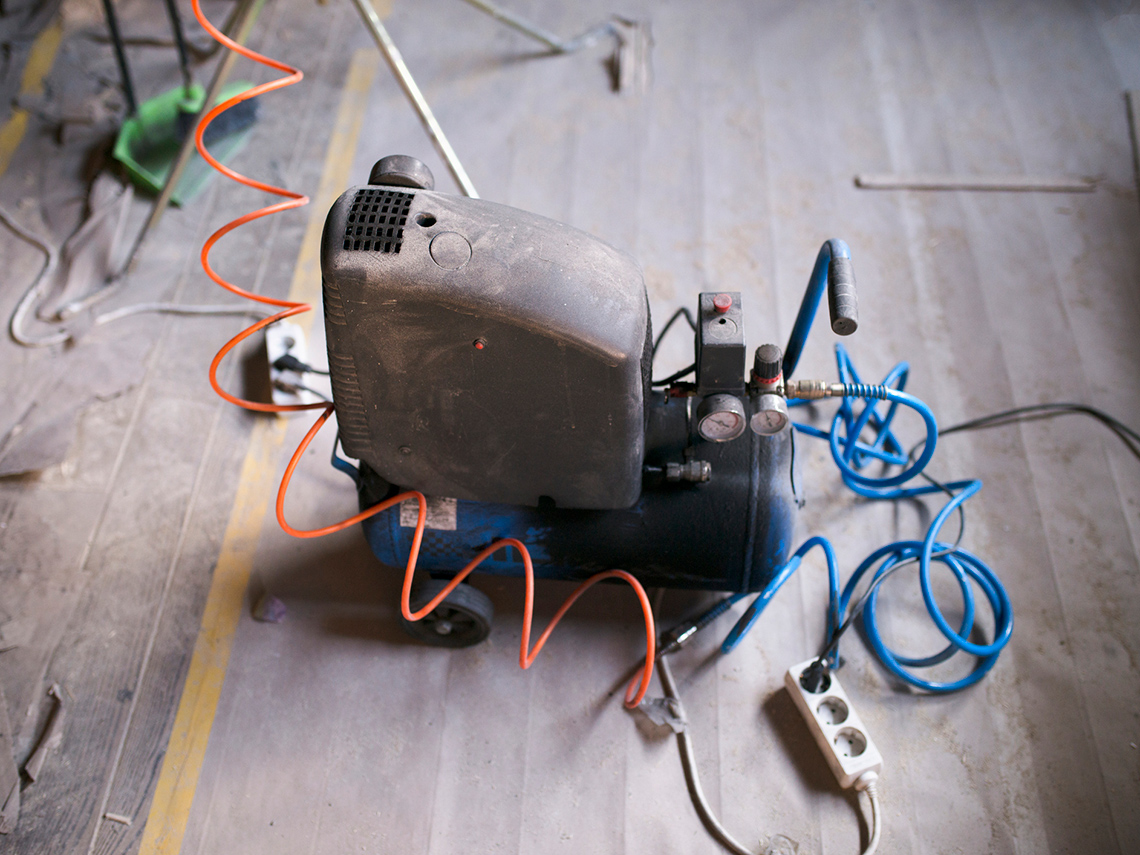 An air compressor with a large metal base, two valves and a series of wires and electrical cords.