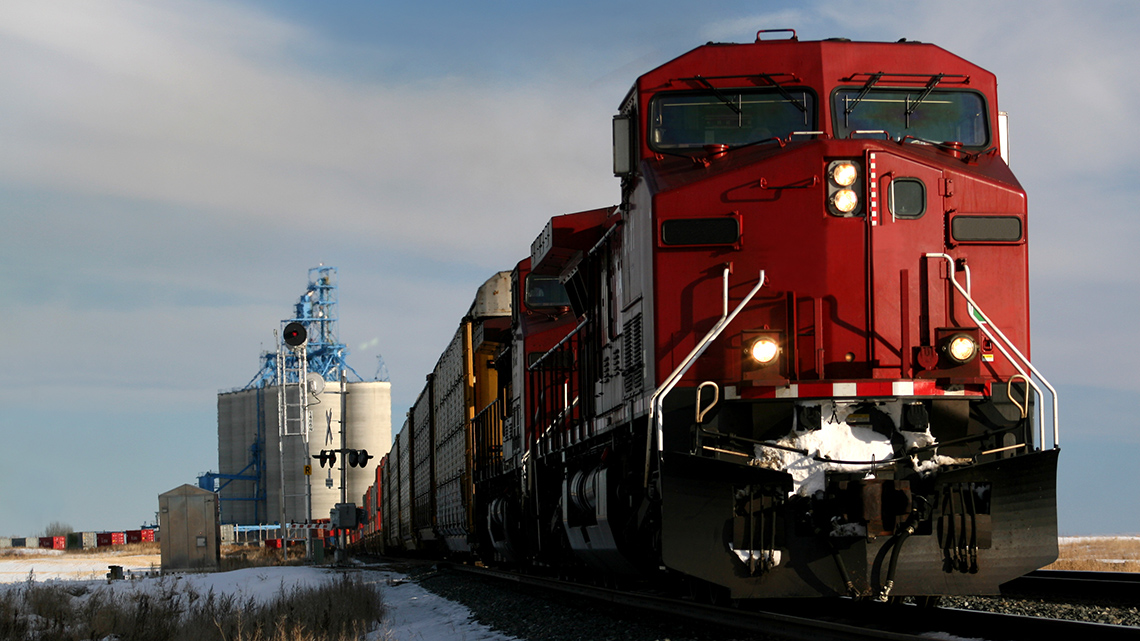 A red train on the tracks in Alberta with grain silos in the background