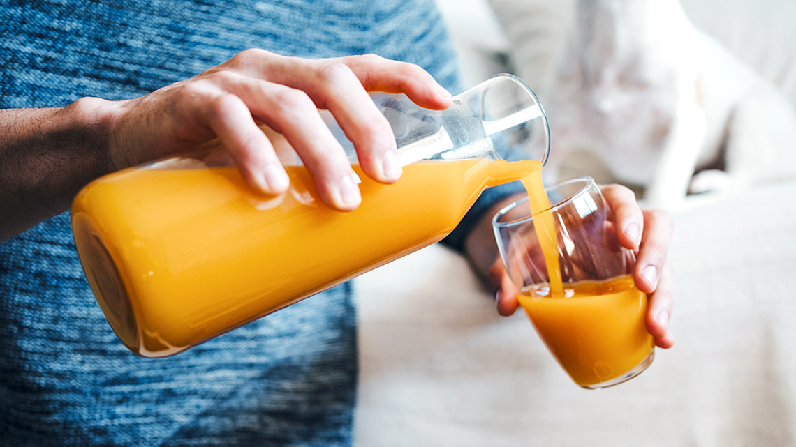 A person is pouring orange juice into a glass.