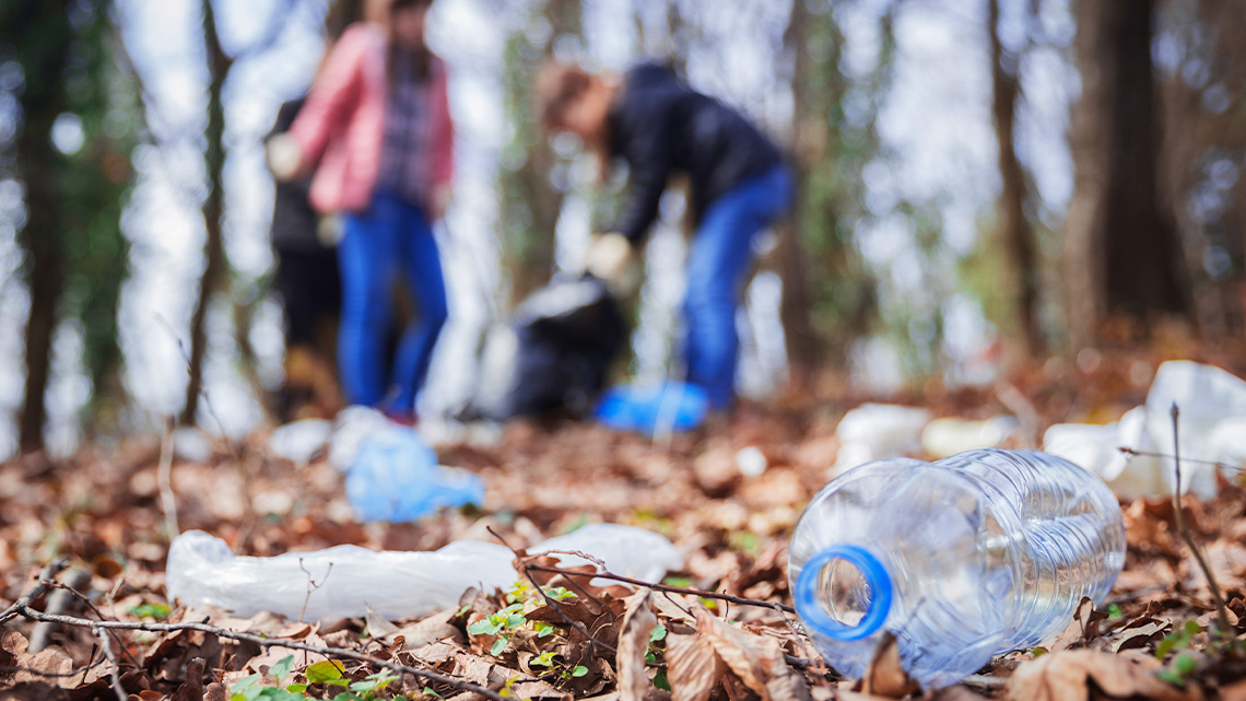 Two learners are cleaning up plastic litter including water bottles in a natural area.