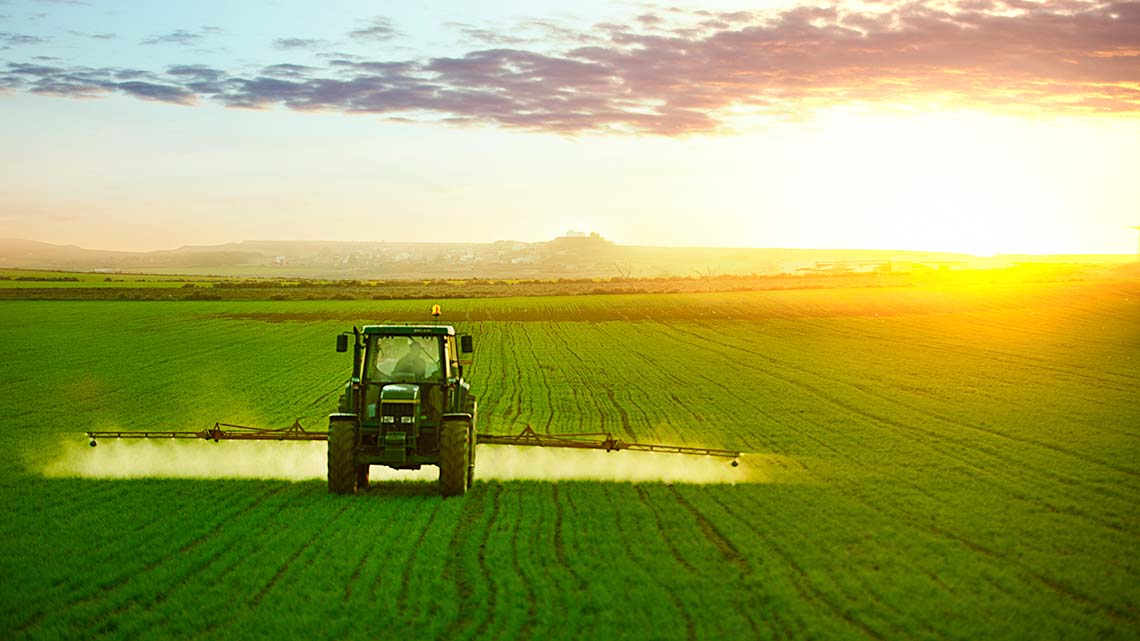 Pollution A tractor driving through a field spraying pesticide on crops.