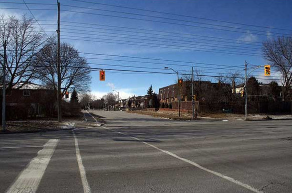 A colour photo of a paved street with power lines and buildings.