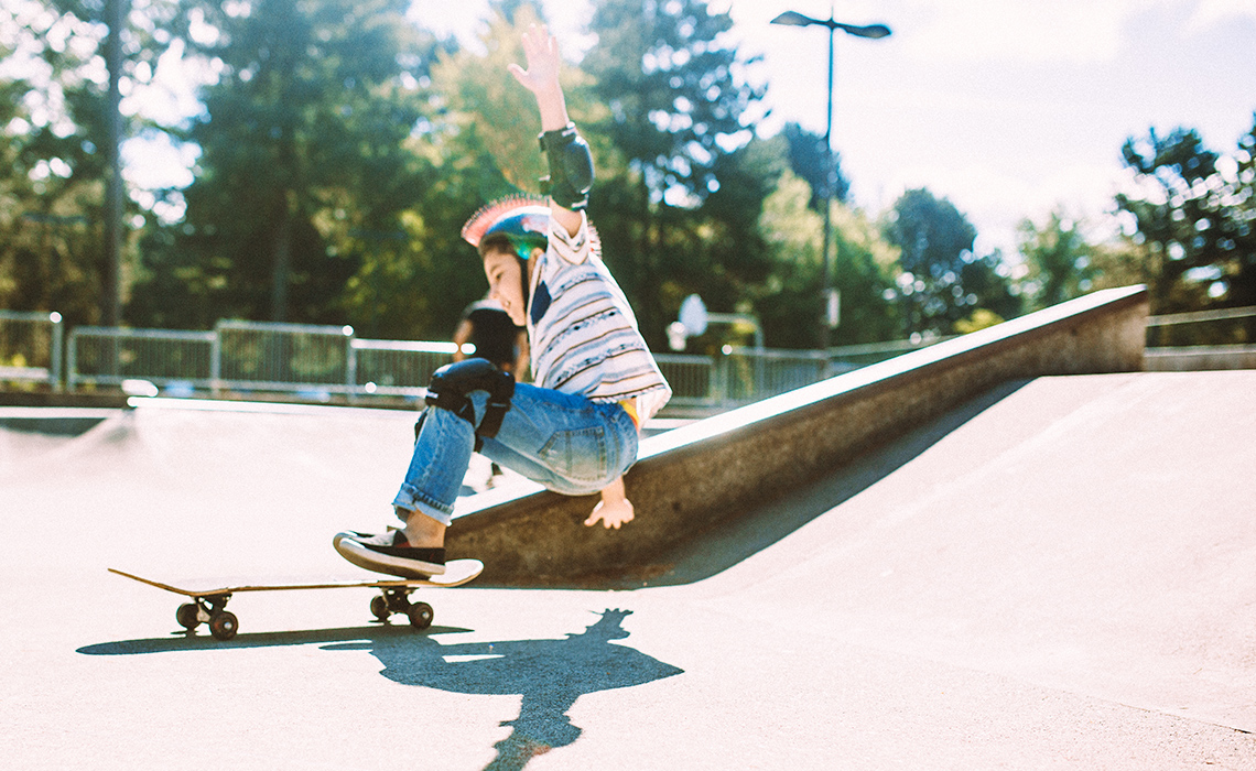 A skateboarder at a skate park falling to the ground after grinding on a staircase railing.