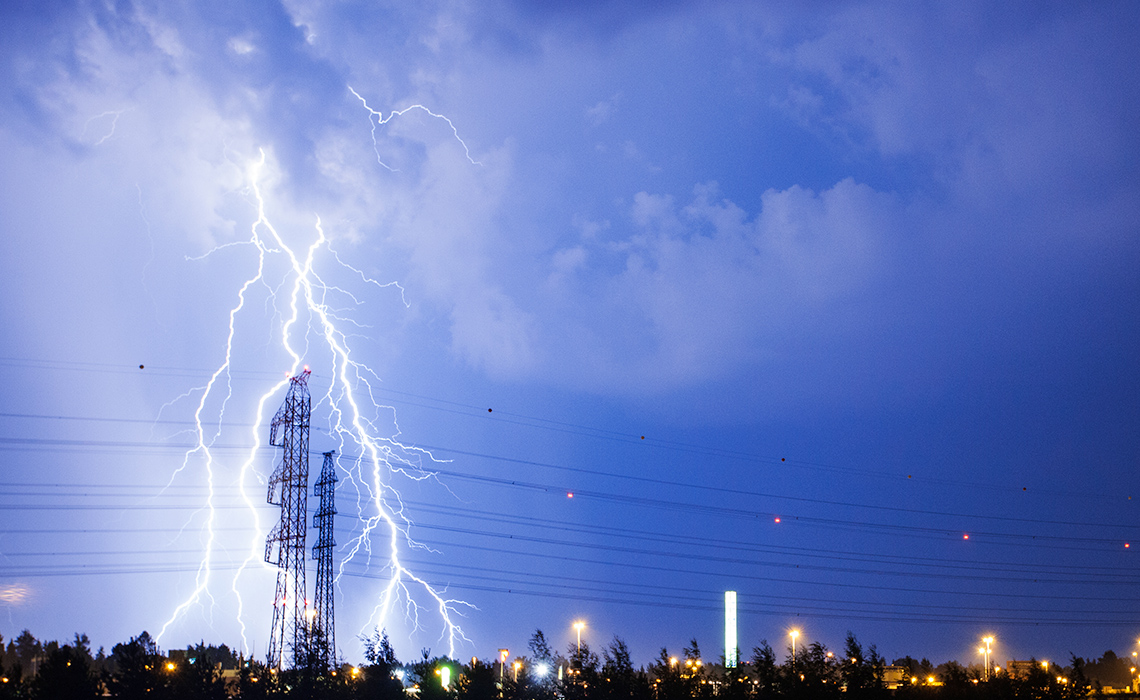 A big bolt of lightning forks out of storm clouds and strikes the ground in a neighbourhood.