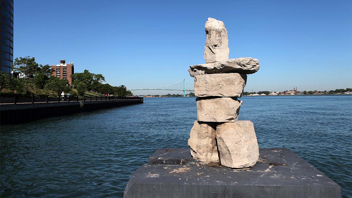Large stones piled in the shape of a person on a platform in water near a shore.