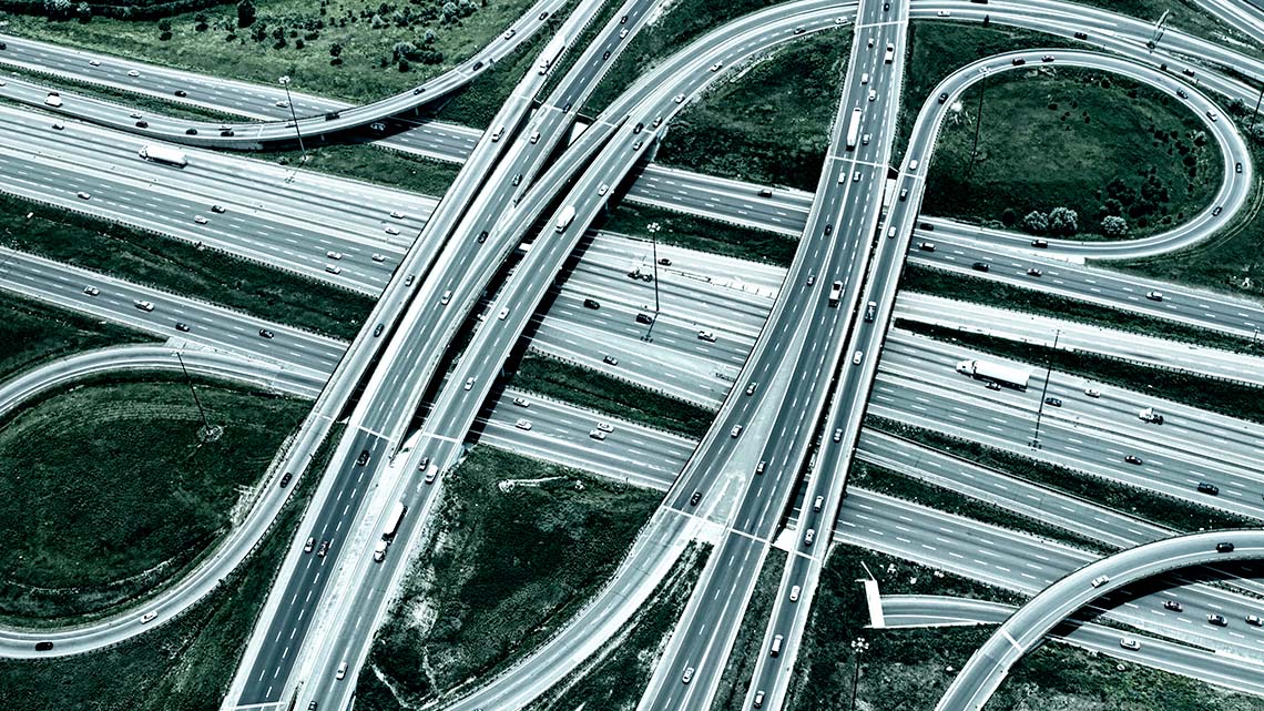 An overpass with on-ramps and off-ramps connecting two intersecting six-lane highways.