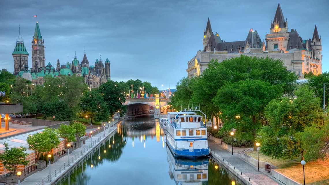 A canal through a city with walkways and buildings on both sides, and a bridge in the distance.
